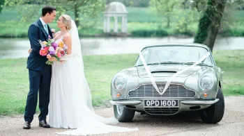 Bride and Groom holding each others next to the Astoin Martin decorated with white ribbons