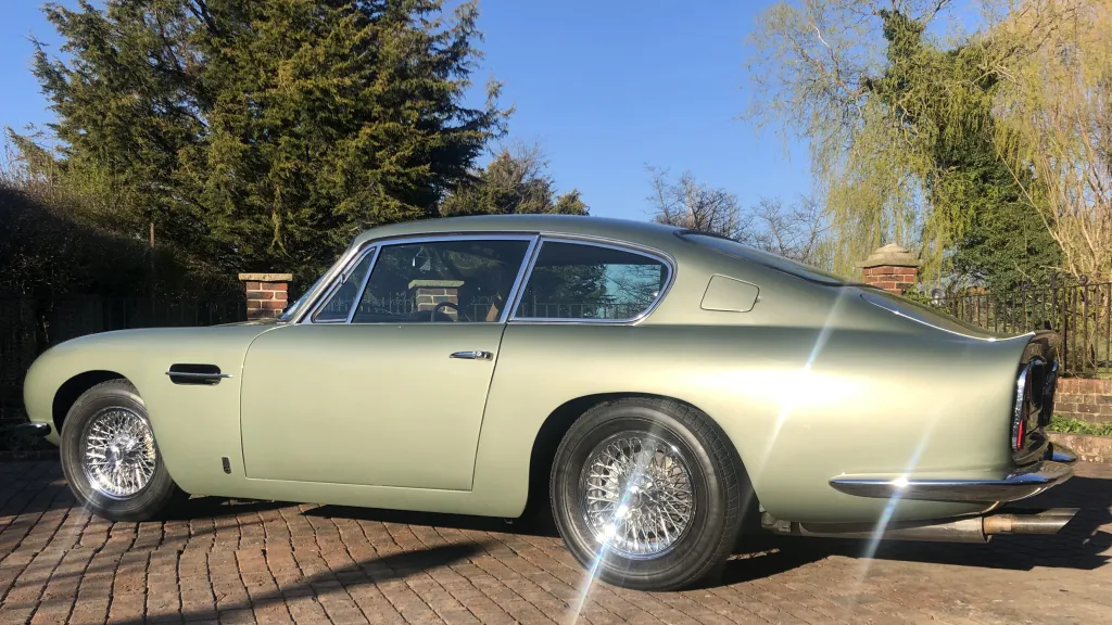 Rear left view of Aston Martin DB6 in pale metallic green and shiny chrome spokes wheels