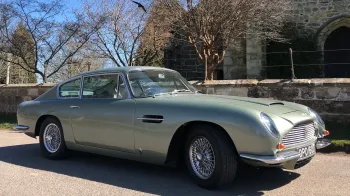 Right Side view of Classic Aston Martin DB6 in Pale metallic green and chrome spokes wheels in front of a church