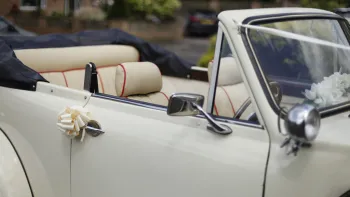 Black soft-top roof open on Ivory Beauford showing cream leather interior. Ivory bow on the door handle