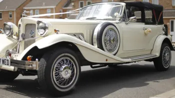 Front left side view of Vintage Beauford decorated with white ribbbon, spare wheel mounted on the side of the vehicle with thin white wall tires.
