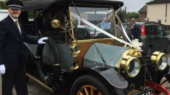 Close up view of Vintage Oakland with its chauffeur standing by the vehicle wearing s full suit with hat and white gloves