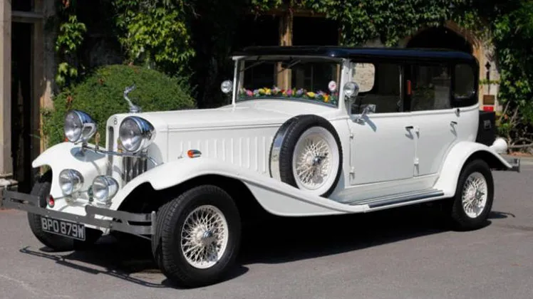 White vintage Beauford with black roof, white spokes wheels parked outside wedding venue