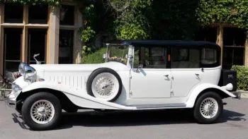 Left siode view of White vintage Beauford with black roof, white spokes wheels and spare wheel mounted on the side of the vehicle