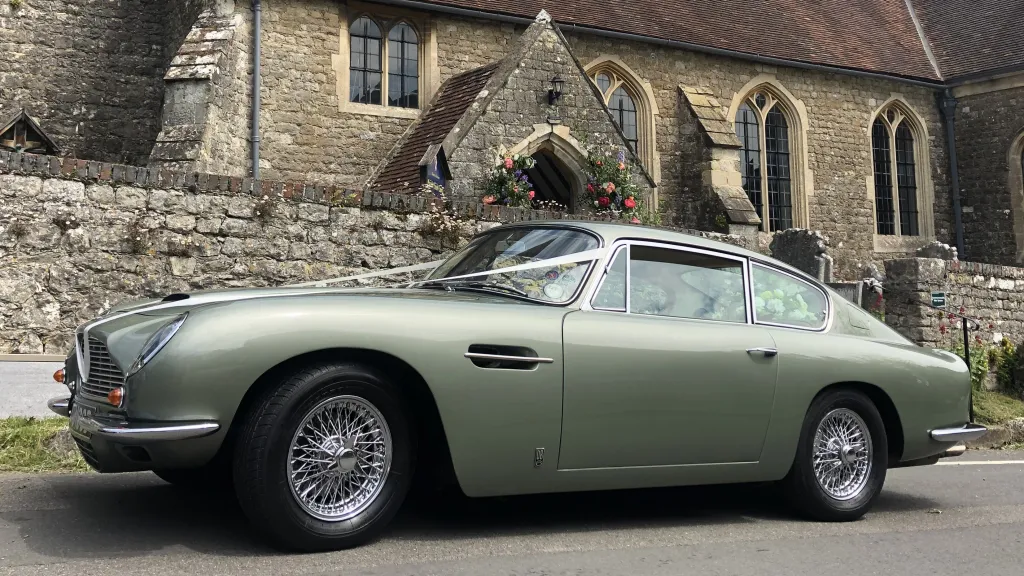 Left side view of Classic Aston Martin DB6 decorated with white ribbons in front of a wedding church
