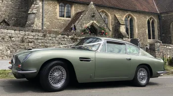 Left side view of Classic Aston Martin DB6 decorated with white ribbons in front of a wedding church