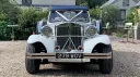 Full front view of Beauford Convertible with large 30s style headlights, chrome grill and bumper dressed with white ribbons in "V-shape" position across the bonnet