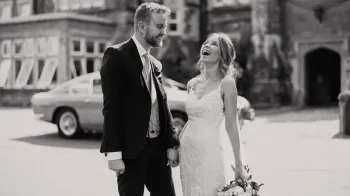 Black and White photo of newly wed couple with Aston Martin ion the background