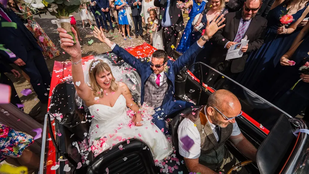 Ford Mustang Convertible wavbing to their wedding guests from inside the Mustang with roof down
