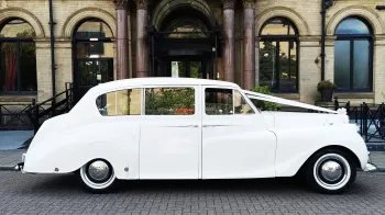 Full right side view of White Classic Austin Princess Limousine with chrome wheel caps. White ribbons and bow accross the front bonnet.