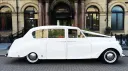 Full right side view of White Classic Austin Princess Limousine with chrome wheel caps. White ribbons and bow accross the front bonnet.