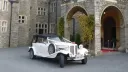 Ivory Beauford Convertible with white ribbons parked in front of wedding venue
