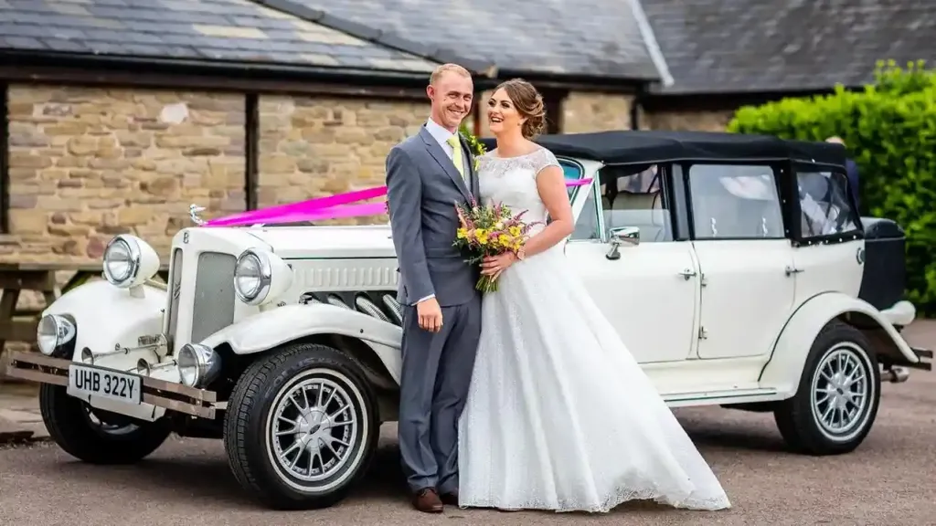Bride and groom standing in front of Beauford convertible decorated with Pink ribbons