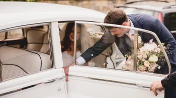 Groom helping bride getting out of Classic Rolls-Royce Silver Cloud