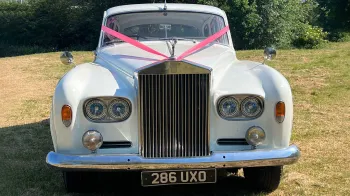 Full front view of classic rols-royce silver cloud with twin headlight, red ribbons and large chrome radiator