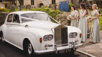 Rolls-Royce Silver Cloud dressed with white ribbons and 3 bridesmaids standing by the vehicle