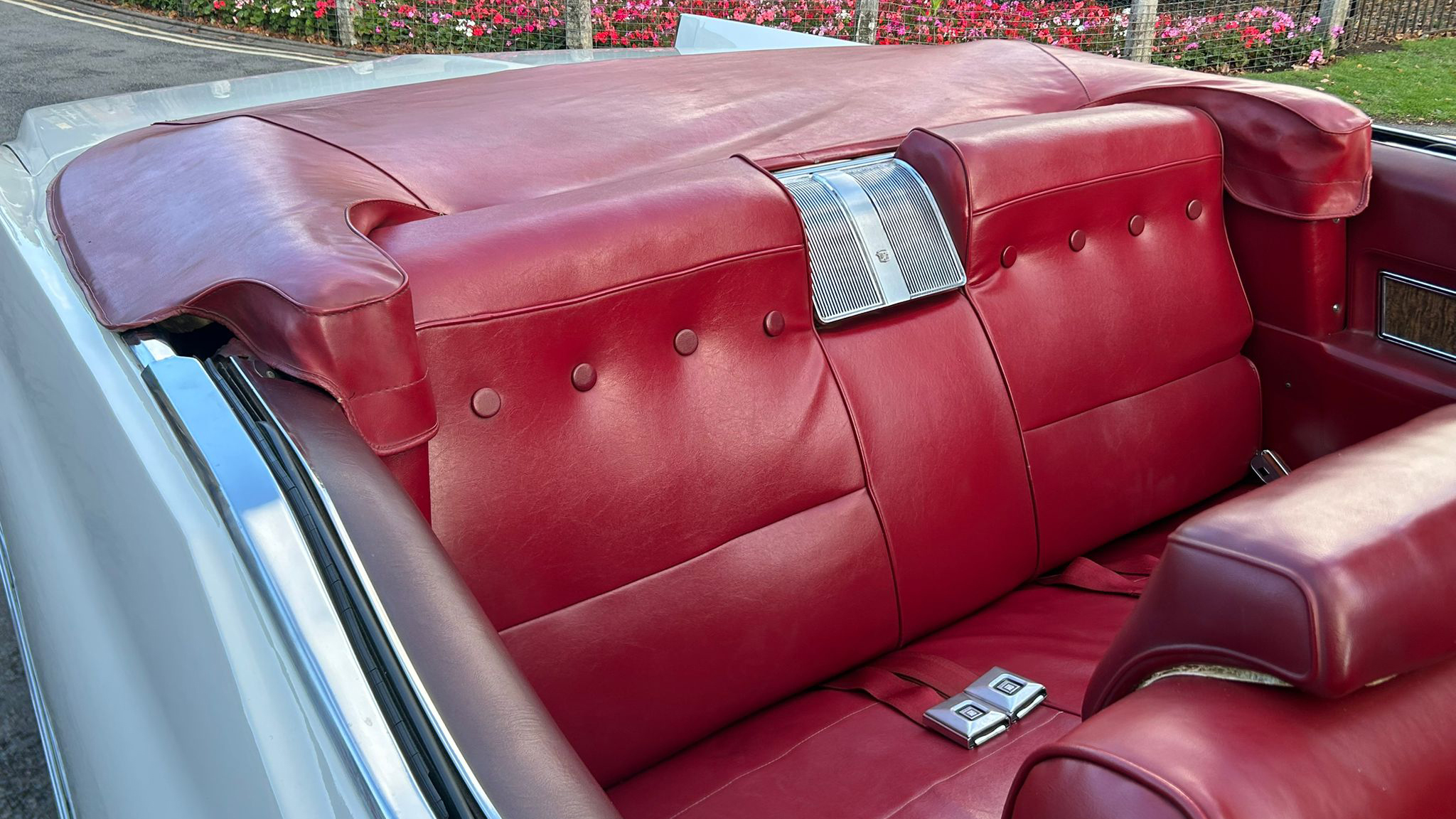 Rear seats of a 1970 Cadillac Coupe DeVille convertible showing buttoned red leather upholstery with some chrome work