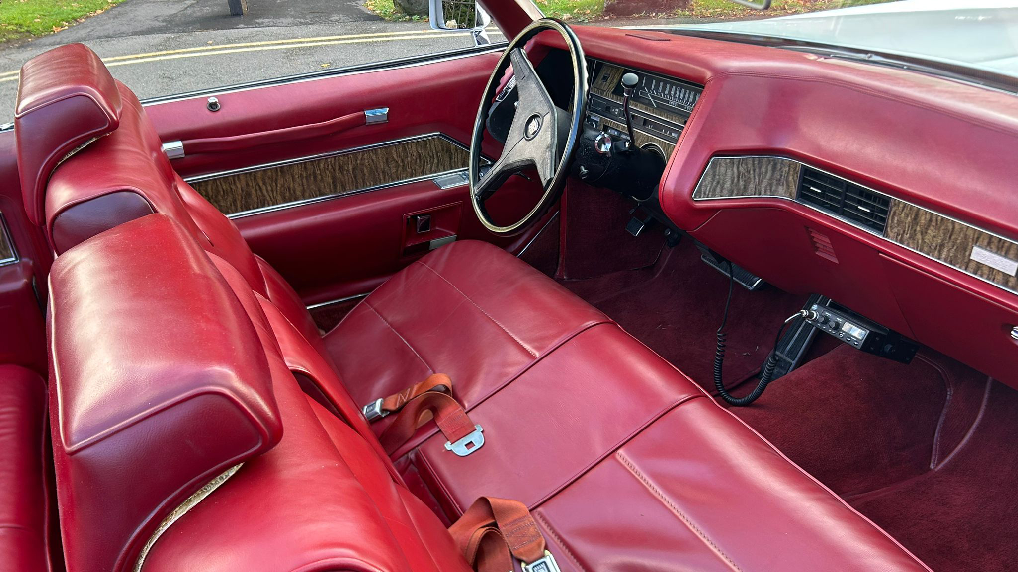 Driver’s view inside a 1970 Cadillac Coupe DeVille showing red leather seats, matching dashboard, and classic chrome trim.