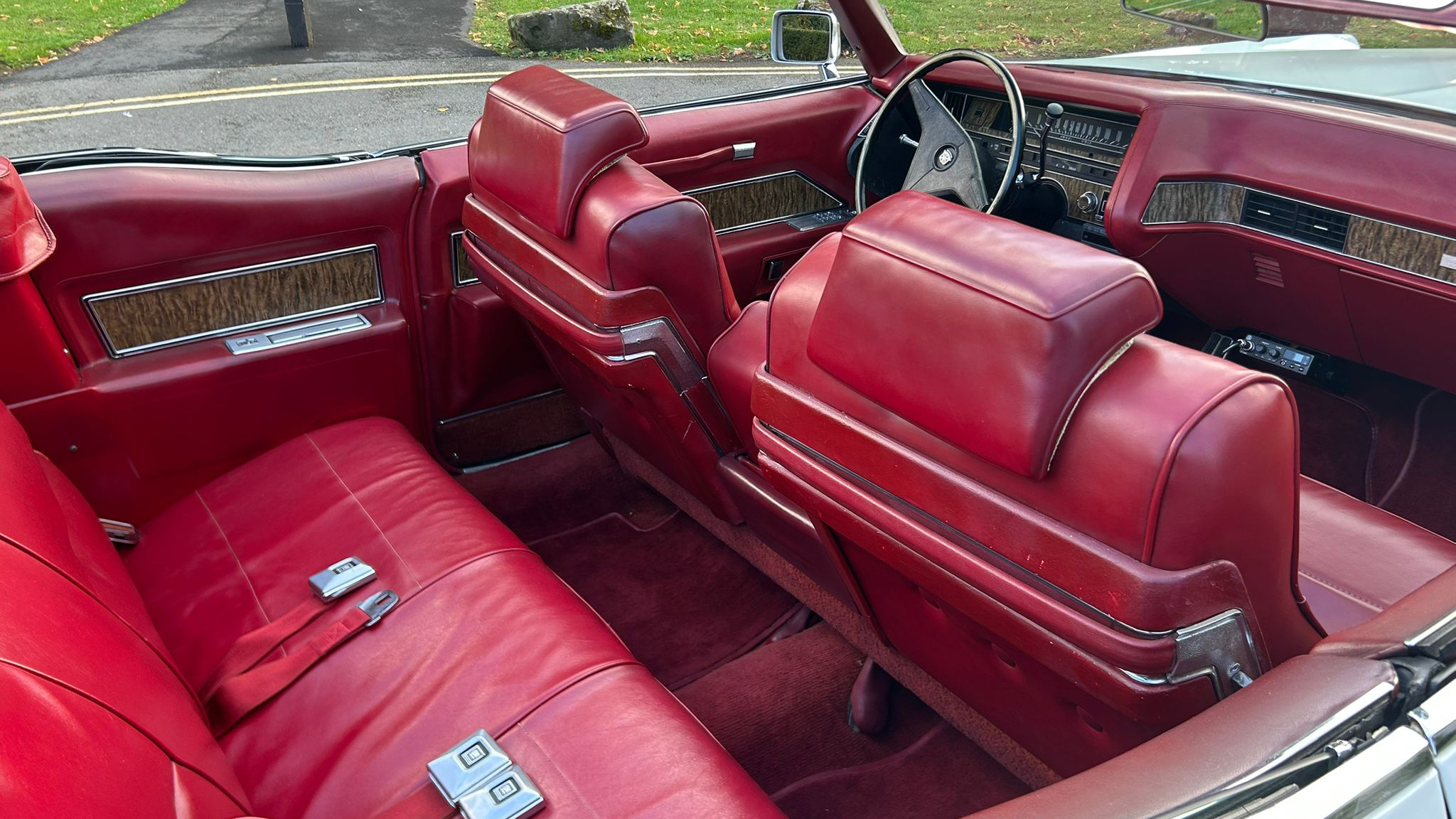 Front and rear seats of a 1970 Cadillac Coupe DeVille featuring luxurious red leather upholstery and chrome detailing.