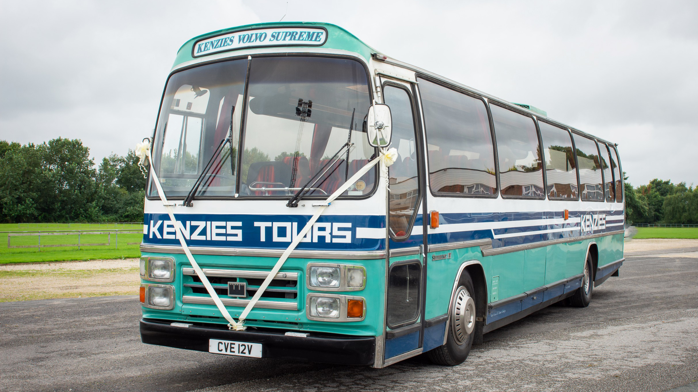 Front angled view of a vintage turquoise and cream single-decker bus with “Kenzies Tours” signage, parked in open countryside in Yorkshire.