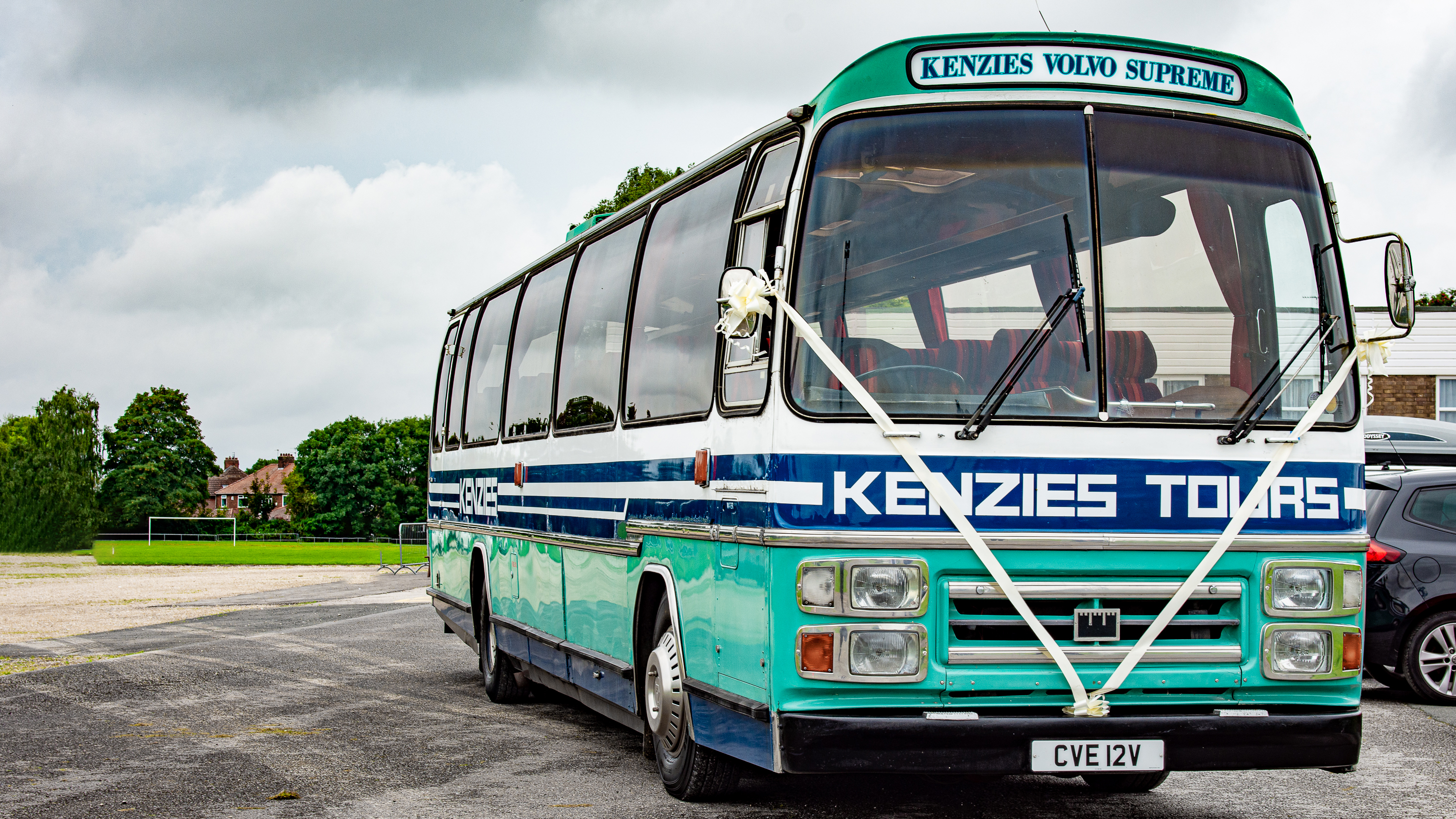 Vintage turquoise single-decker bus decorated for a wedding, photographed on a quiet road surrounded by greenery in Yorkshire.