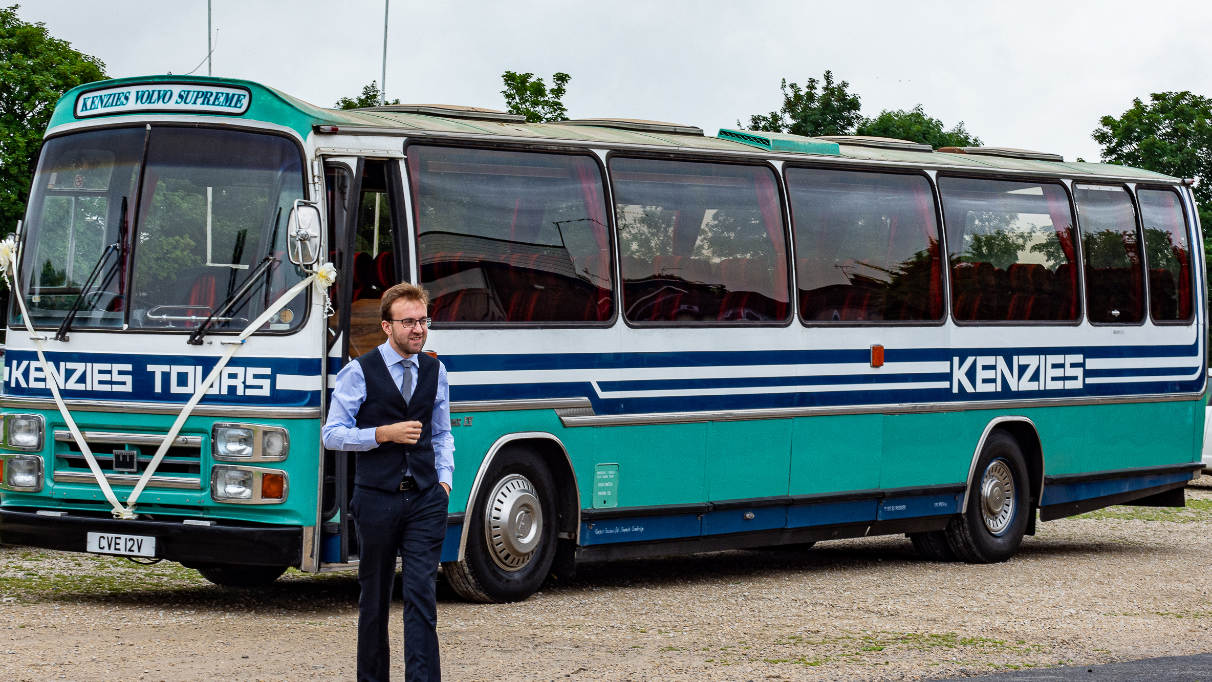 Wedding guests boarding a turquoise single-decker vintage bus outside a stone church, ideal for group wedding transport in Yorkshire.